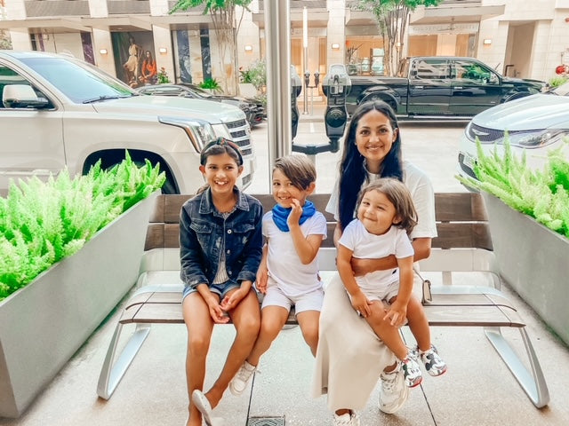 Mom sitting with her 3 kids on a bench outside, all smiling.