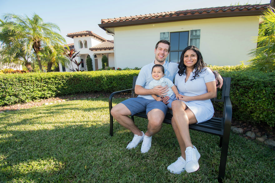 Family of three sitting on a bench outside together, smiling.