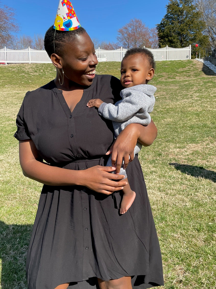 Mom wearing a party hat, holding her son in her arms looking lovingly at him. Standing outside in the sun.