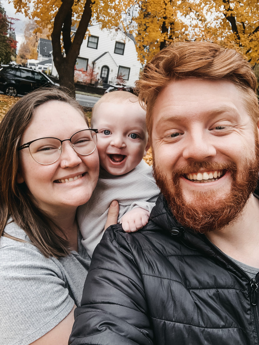 Happy family of 3 huddled together outside, smiling.