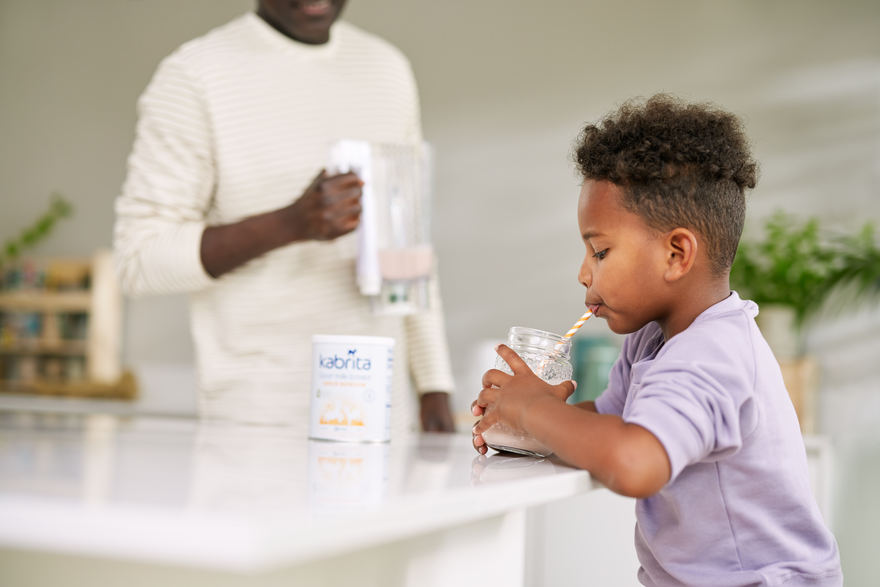 Little boy sitting at the table, drinking a smoothie with Kabrita Junior.